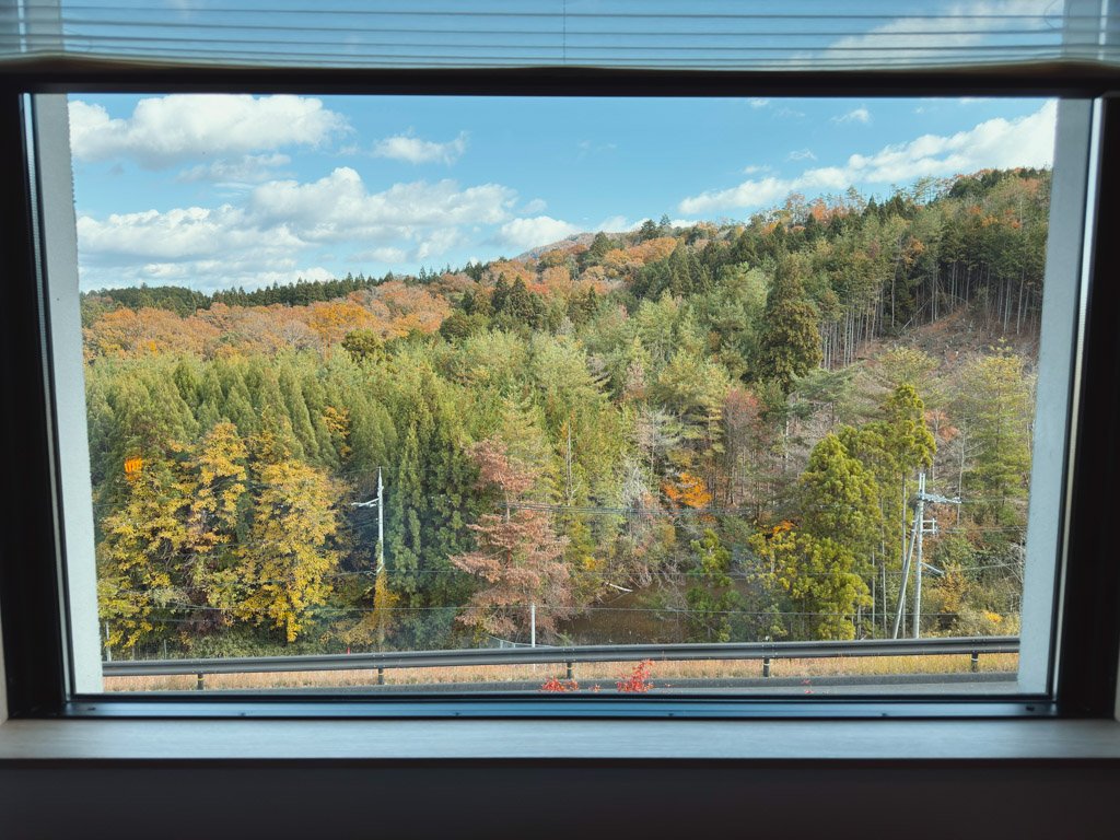 客室の窓から見える自然豊かな景色。山々が紅葉し、美しい秋の風景が広がっています。