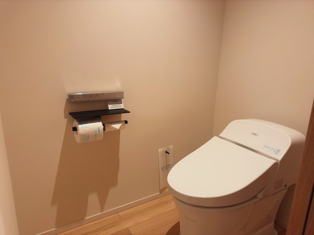 客室内のトイレ。ウォシュレット機能付きで、壁には操作パネルとトイレットペーパーホルダーが備え付けられています。