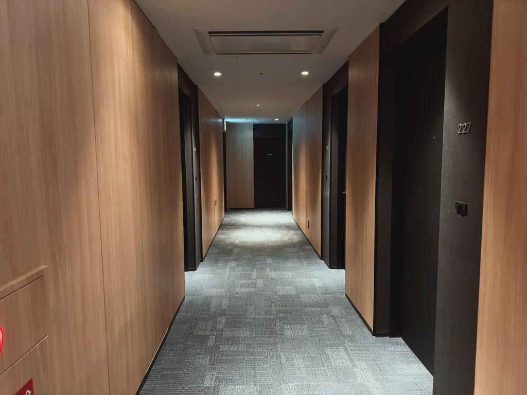 ホテルの客室フロアの廊下。シンプルなデザインの廊下が奥へ続き、部屋番号「227」が見えます。