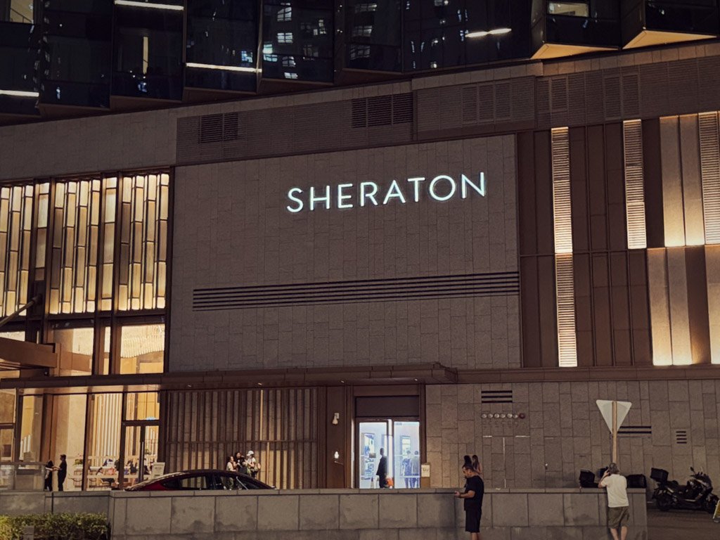  フォーポイントバイシェラトン香港、東涌の建物の一部。隣接する「SHERATON」のロゴがライトアップされている外観。 