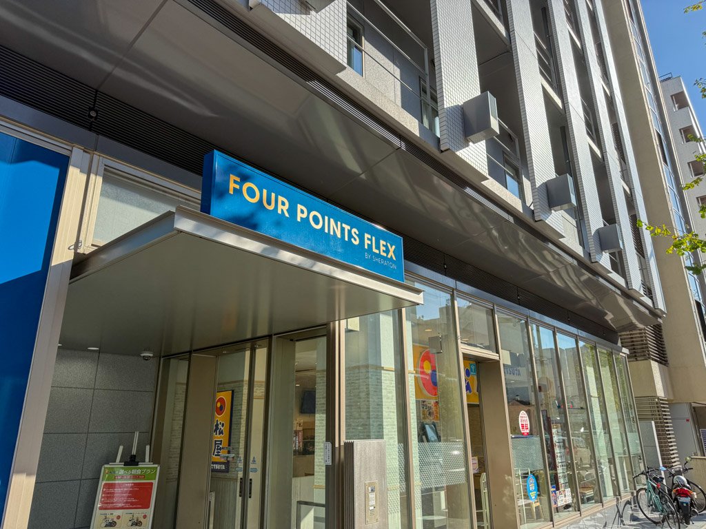 フォーポイント フレックス by シェラトン 神戸三宮のエントランス部分。青い看板に「FOUR POINTS FLEX」のロゴが目立ち、ガラス張りの入り口がモダンな雰囲気を演出しています。