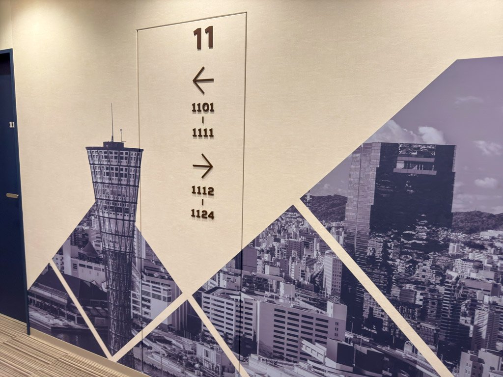 フォーポイント フレックス by シェラトン 神戸三宮の廊下にある壁面デザイン。神戸の街並みやポートタワーが描かれ、部屋番号の案内が配置されている。
