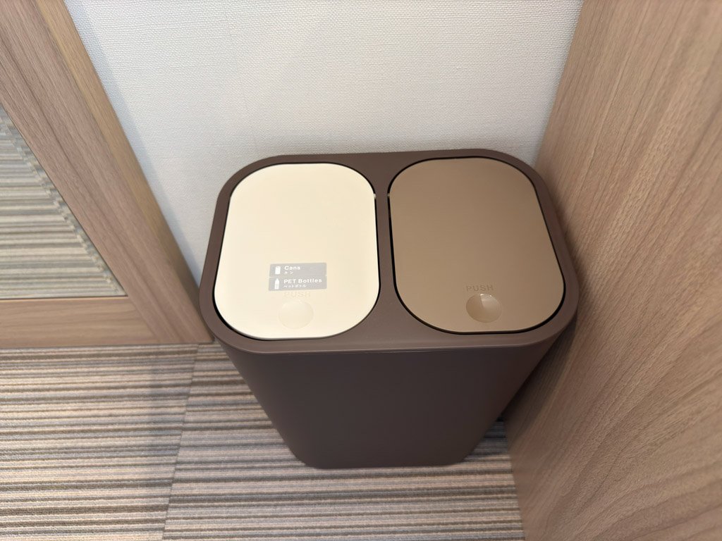 フォーポイント フレックス by シェラトン 神戸三宮の客室内にある分別ごみ箱。白と茶色の2つのフタがあり、片方には「Cans / PET Bottles」とラベルが記載されている。