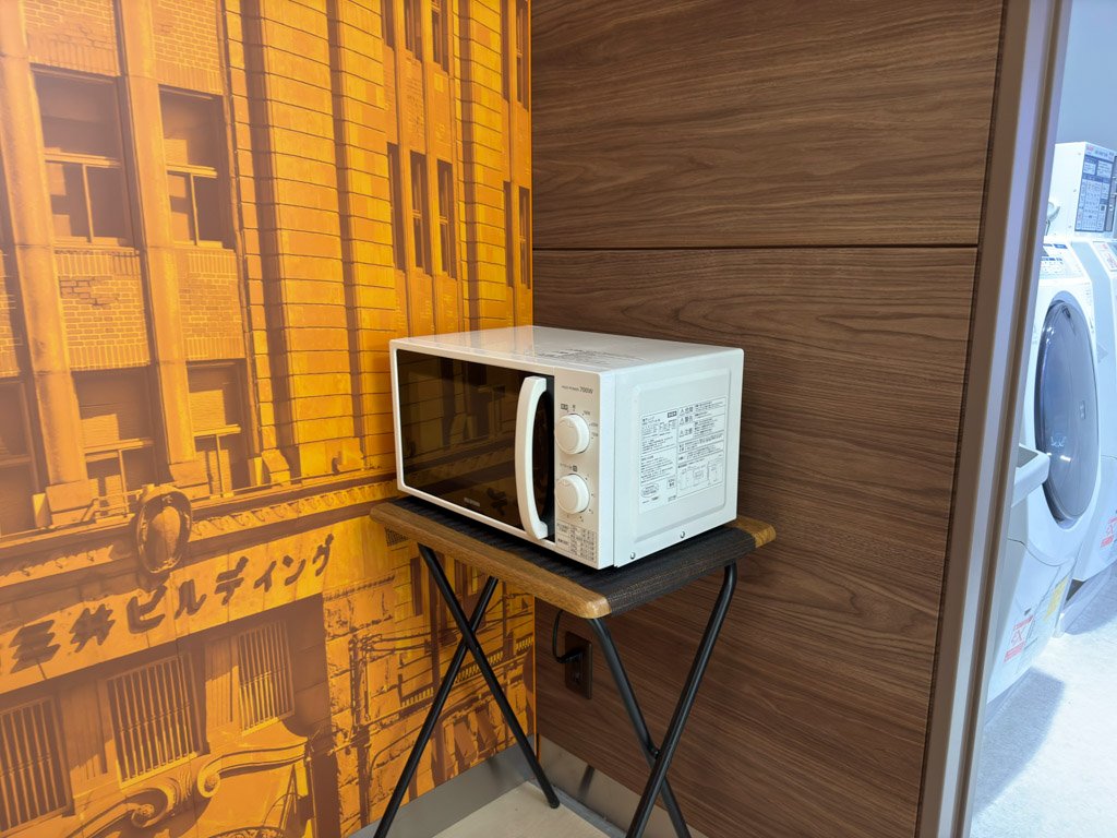 フォーポイント フレックス by シェラトン 神戸三宮の1階に設置された電子レンジ。壁にはレトロなデザインの装飾が施され、隣にはランドリー設備が見える。