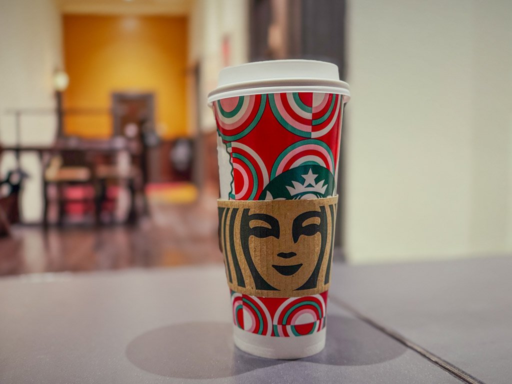 スターバックスのカップ。ホリデーシーズンらしい赤と緑のデザインが印象的で、テーブルの上に置かれています。