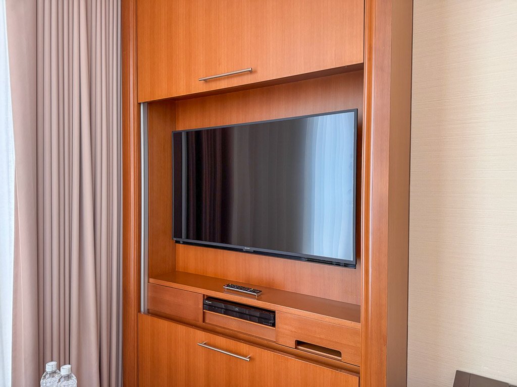  セントレジス大阪の客室にあるテレビは、洗練された木製キャビネットに収められ、クラシックなデザインが特徴です。基本的な視聴機能は備えていますが、解像度や最新のディスプレイ技術の観点では、現代の標準には及ばないかもしれません。  The in-room television at The St. Regis Osaka is housed within a sleek wooden cabinet, offering a classic design touch. While the TV provides essential viewing options, it may not meet the latest standards in terms of resolution and modern display technology, reflecting a more traditional aesthetic.  