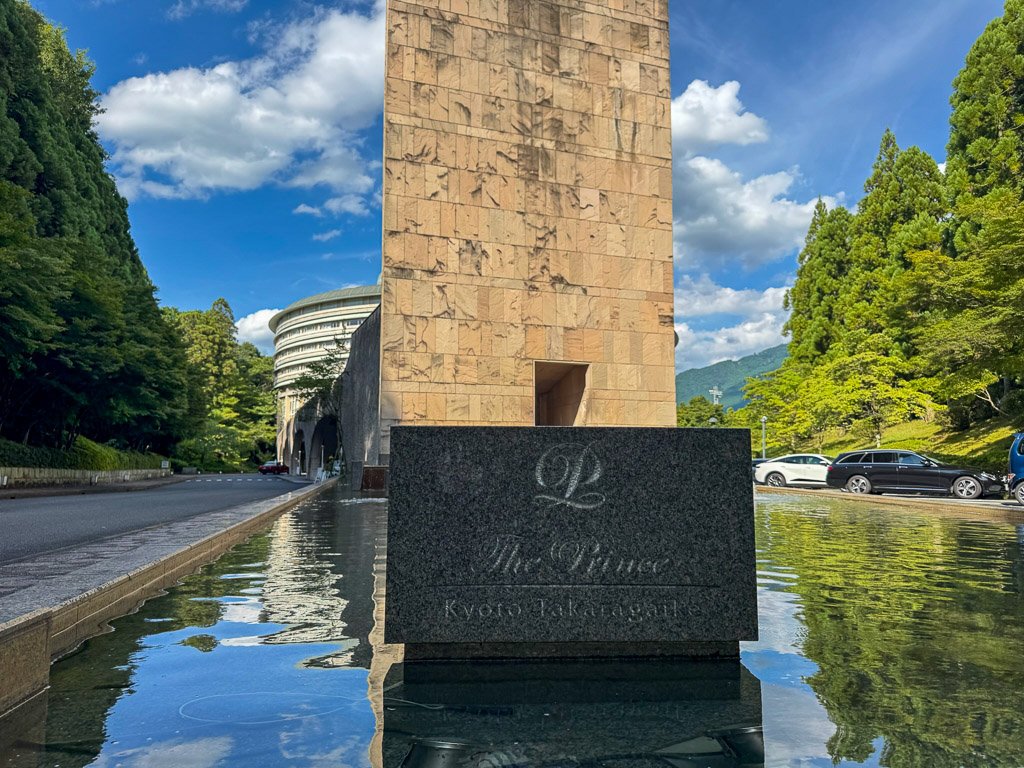 石碑に刻まれたホテル名と、背景に広がる緑豊かな景色が印象的です。 