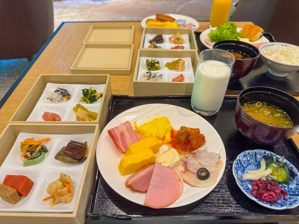  この朝食は、和洋折衷のメニューが豊富に揃っており、彩り豊かな料理が目を引きます。左側の小鉢には、季節の食材を使った繊細な和食の前菜が並び、バランスの取れた味わいが楽しめます。主菜としては、卵料理やハムなどがプレートに盛り付けられ、洋食の要素も取り入れられています。さらに、ご飯と味噌汁、漬物が添えられており、日本の伝統的な朝食の魅力を感じさせる一食です。ミルクやジュースなど、ドリンクも充実しており、朝から満足感の高い食事がいただけます。 