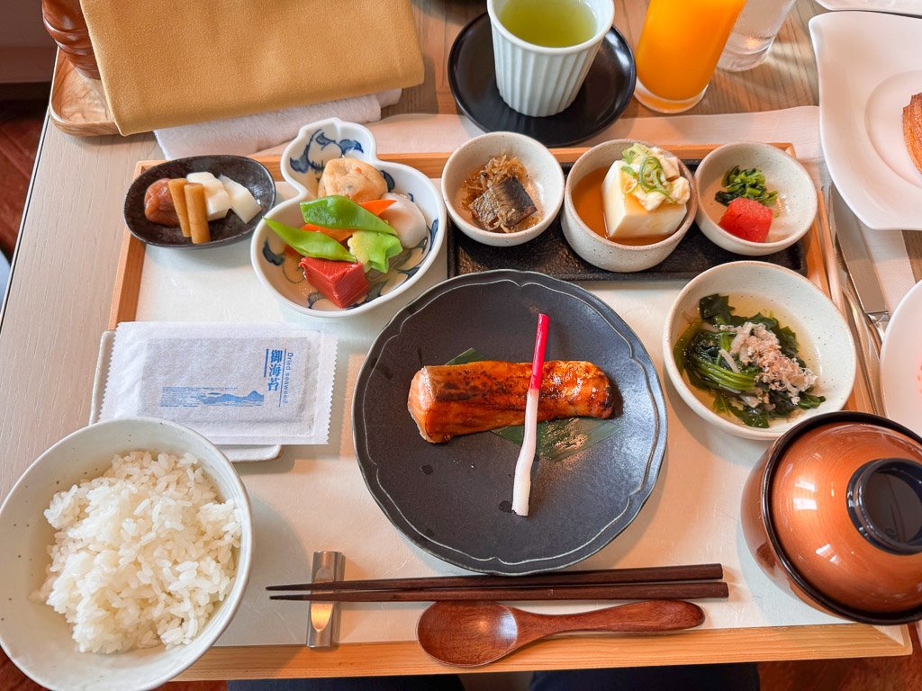  セントレジス大阪のレストラン「ラ・ヴェデュータ」で提供される和風朝食セット。さまざまな伝統的な料理がトレーに美しく盛り付けられています。  A Japanese-style breakfast set at La Veduta, St. Regis Osaka, featuring a variety of traditional dishes presented elegantly on a tray. 