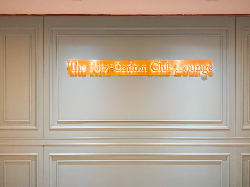 壁に取り付けられた「The Ritz-Carlton Club Lounge」のサイン。サインは暖かい光で照らされ、クラシカルでエレガントなフレームに囲まれた壁に掲げられています。高級感のあるデザインが特徴です。 