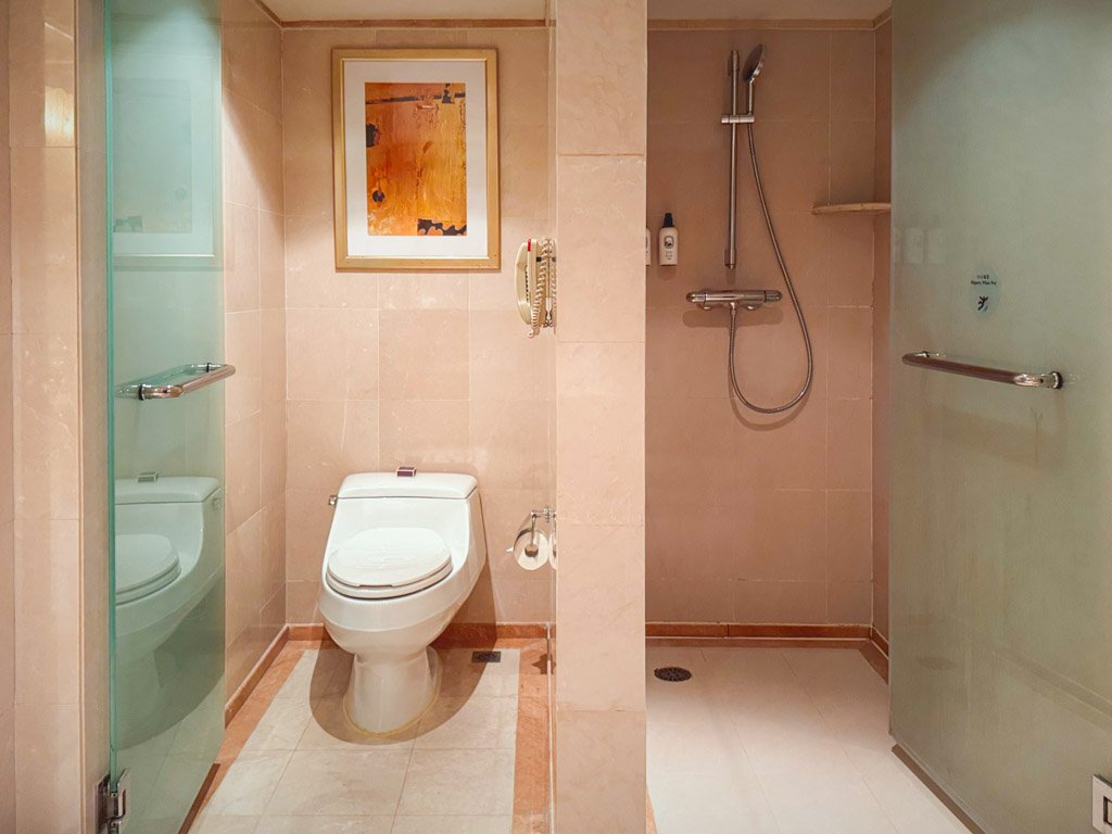 バスルーム内のトイレとシャワールームが並んで配置され、ガラスの仕切りで区切られています。清潔感のある空間で、壁にはアートが飾られています。シャワーには固定式のシャワーヘッドが備えられ、使いやすさが考慮されたデザインです。 