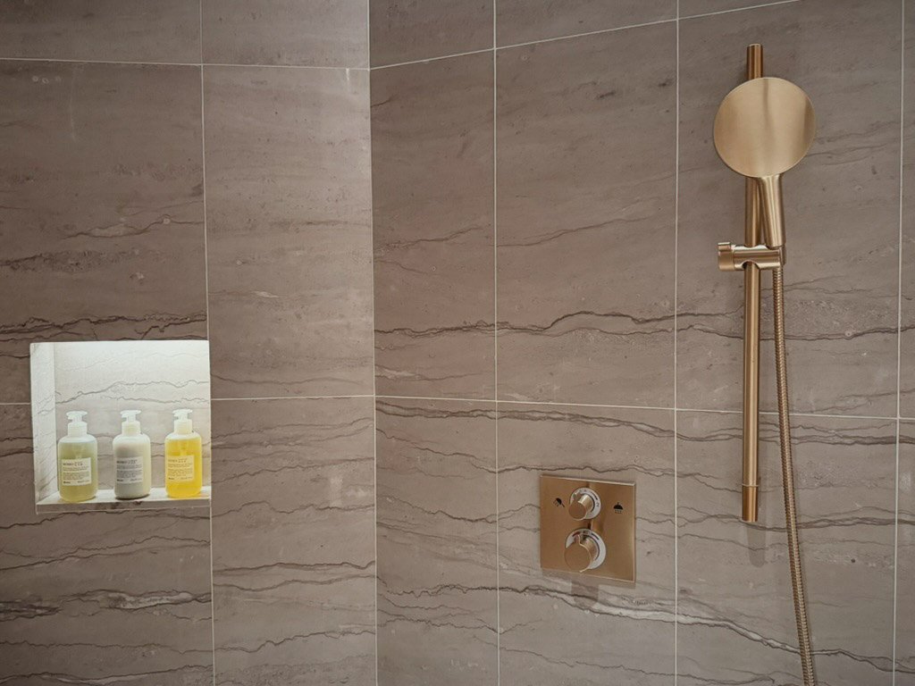  シャワールームの壁には、シンプルでスタイリッシュなゴールドのハンドシャワーが取り付けられています。また、壁のくぼみにはバスアメニティが並んでおり、DavinesのMOMOシリーズのシャンプーやボディソープが揃えられています。 