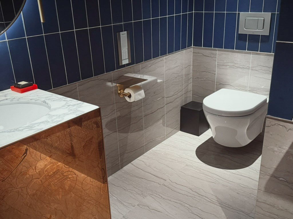 マーベラススイート内の来客用トイレ。ブルーとグレーのタイルがシックな雰囲気を醸し出し、ゴールドのトイレットペーパーホルダーがアクセントになっています。 