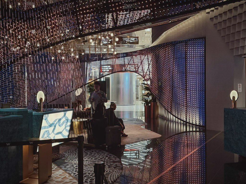  Wマカオ - スタジオシティのロビー待合スペース。LEDライトのカーテンが壁一面に広がり、華やかな雰囲気を演出しています。柔らかな照明が空間を包み込み、ラグジュアリーな待合エリアとなっています。 