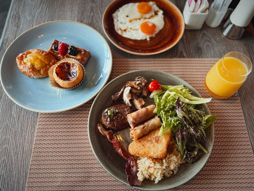  朝食ビュッフェの料理が並ぶテーブル。デザート、サラダ、ハッシュブラウン、スプリングロール、フルーツジュースが用意されています。 