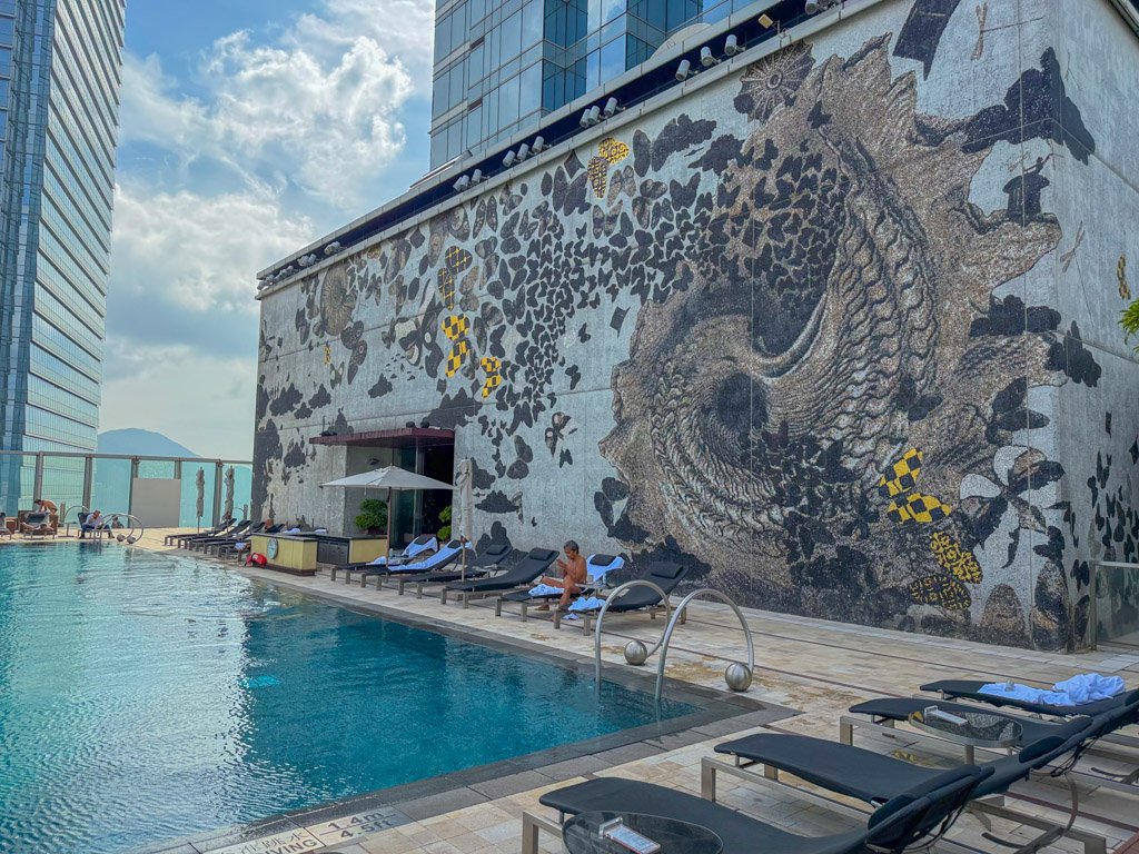  昼間のプールエリア。壁には大きなアートが描かれ、青空が広がる快適な空間。 