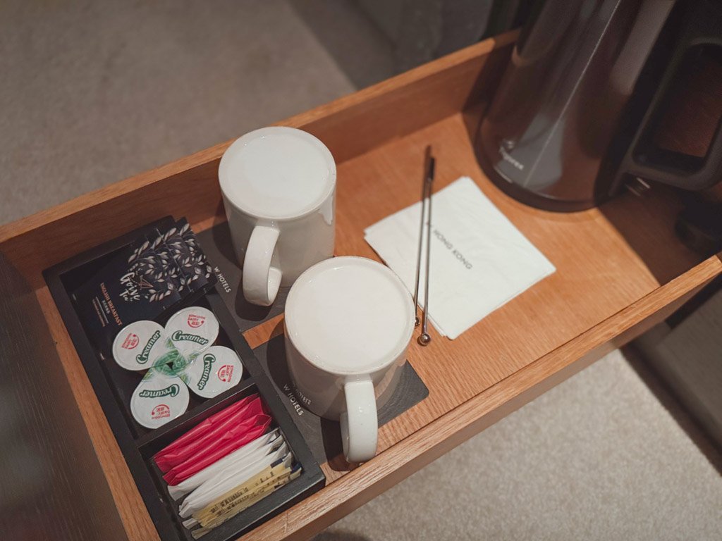  W香港の客室内に用意されたドリンクセット。2つのマグカップ、電気ケトル、紅茶やコーヒー用のミルクや砂糖が木製トレイにきれいに並べられている。 