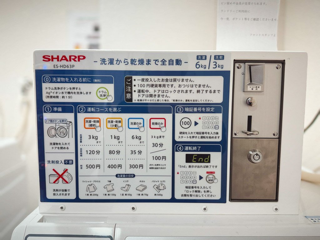 フォーポイント フレックス by シェラトン 横浜駅西のランドリールームに設置された洗濯機の操作パネル。洗濯と乾燥のコースや料金、時間が詳細に説明されており、コイン投入口が横に配置されている。