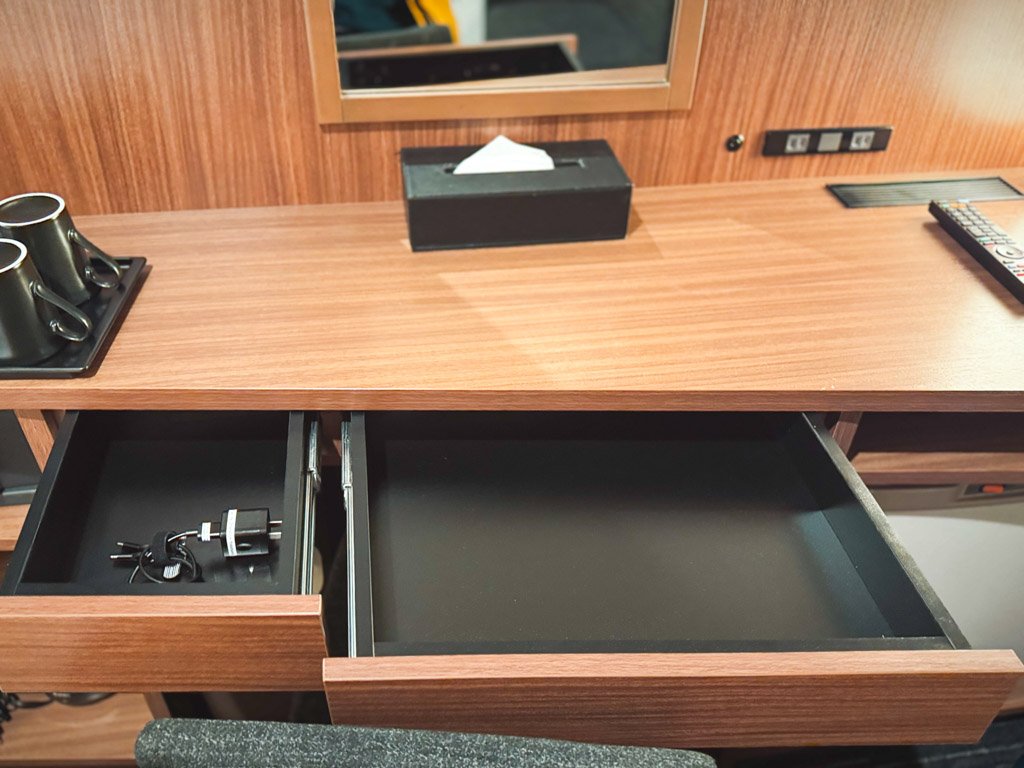 フォーポイント フレックス by シェラトン 横浜駅西の客室デスクの引き出し部分。引き出しには充電器や小物を収納できるスペースがあり、デスク上にはカップやティッシュボックス、コンセントも備え付けられている。