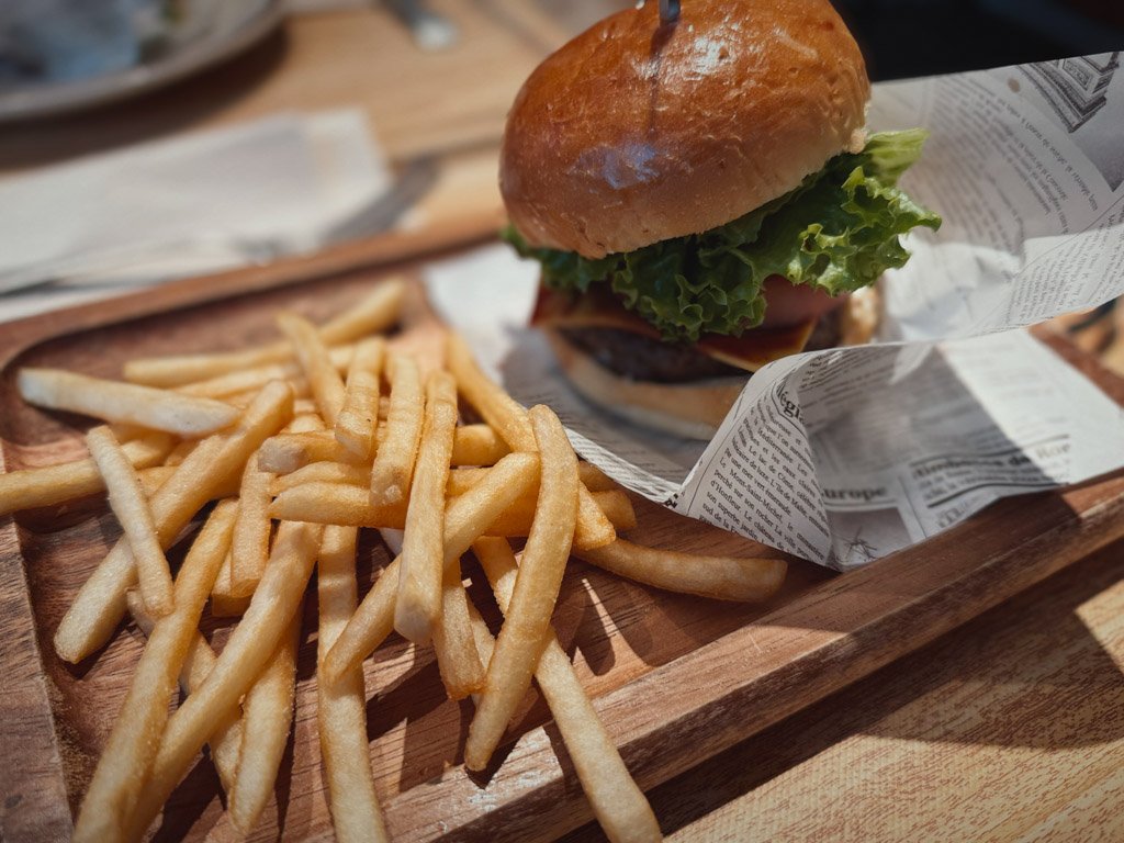 モクシー大阪本町で提供されるハンバーガーセット。ふわふわのバンズに新鮮なレタスとパティが挟まれたハンバーガーが、サクサクのフレンチフライと一緒に木製のプレートに盛り付けられている。
