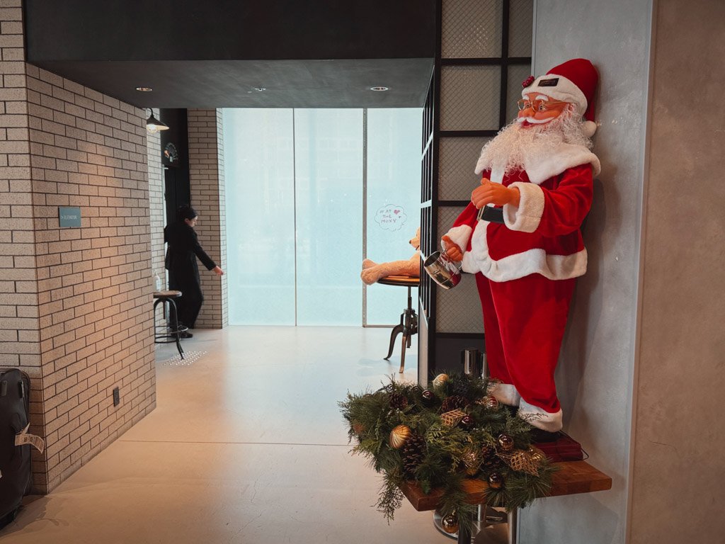 モクシー大阪本町のエレベーター前のスペース。サンタクロースの装飾がクリスマスの雰囲気を演出し、レンガ調の壁とモダンなインテリアが特徴的です。