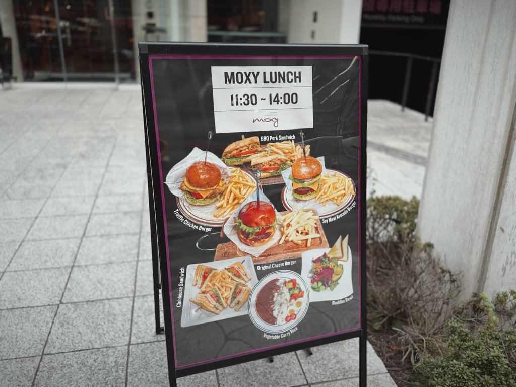 モクシー大阪本町のランチメニュー看板。11:30~14:00の時間帯で提供されるランチのメニュー写真が並び、美味しそうなバーガーやカレー、サンドイッチのイメージが描かれています。