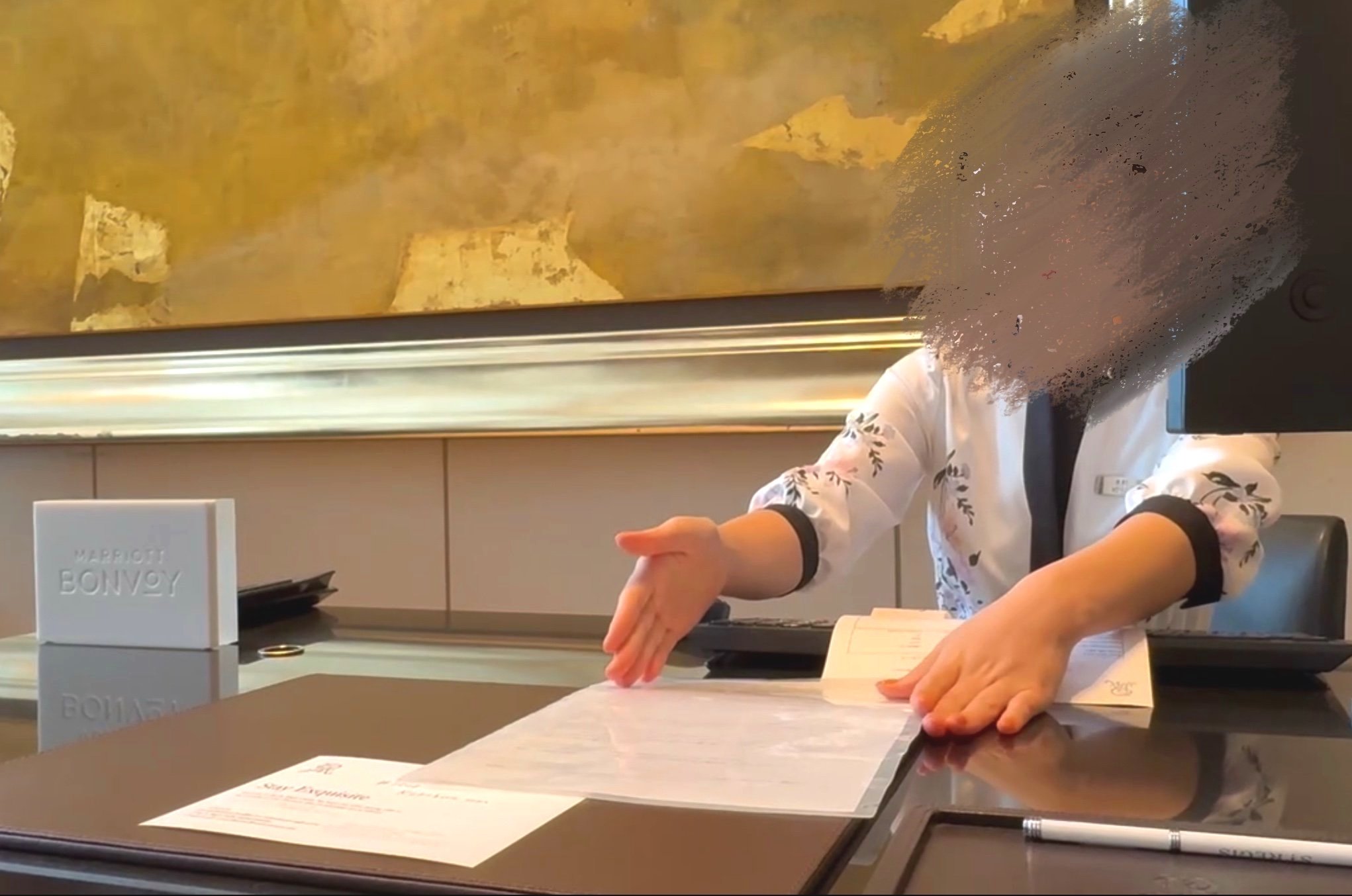  セントレジス大阪のスタッフが、ゲストにチェックイン手続きを説明しています。エクスプレスチェックアウトが利用可能であることを強調しています。  A staff member at The St. Regis Osaka explaining the check-in process to a guest, highlighting the availability of express checkout.  