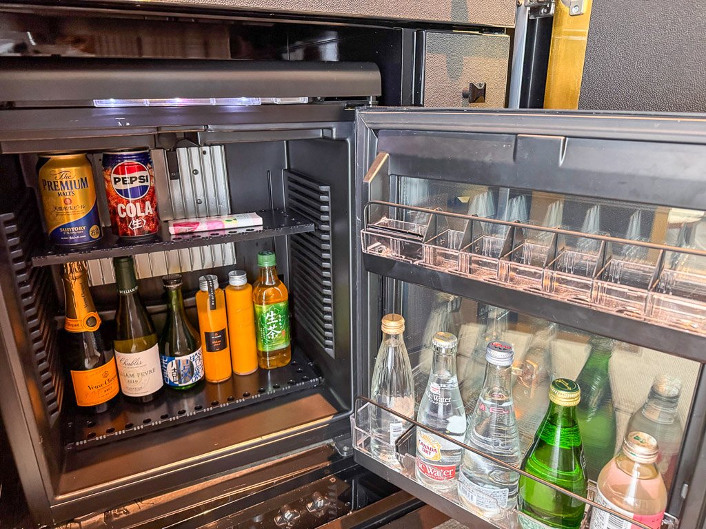  セントレジス大阪のミニバーには、さまざまな高級飲料が揃っています。日本酒やシャンパン、ソフトドリンク、ミネラルウォーターなどが用意されており、客室でのリラックスタイムに多彩な選択肢を提供します。  The minibar at The St. Regis Osaka, stocked with a variety of premium beverages. The selection includes Japanese sake, champagne, soft drinks, and bottled water, offering guests a range of choices to enjoy in the comfort of their room.  
