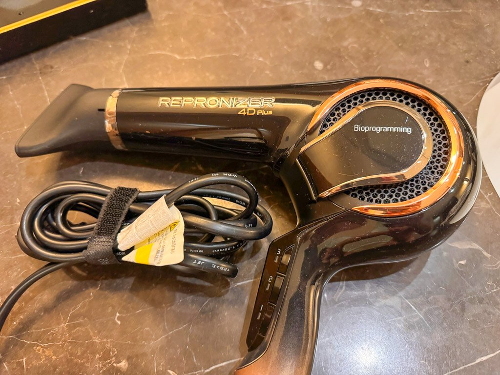  セントレジス大阪のバスルームに備え付けられているRepronizer 4D Plus ヘアドライヤーのクローズアップ。この高級デバイスは、乾かしながら髪質を改善することを目的としたバイオプログラミング技術で知られています。  A close-up of the Repronizer 4D Plus hair dryer provided in the bathroom at The St. Regis Osaka. This high-end device is known for its Bioprogramming technology, which aims to improve hair quality while drying.  