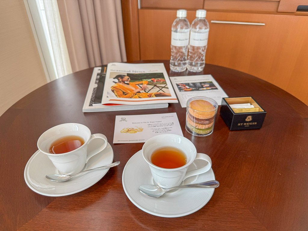  セントレジス大阪では、ウェルカムドリンクとして紅茶を提供してくれました。テーブルには二杯の紅茶、クッキーの詰め合わせ、そしてホテルに関する情報がセットされており、到着したゲストを温かく迎える居心地の良い雰囲気が感じられます。  A warm welcome at The St. Regis Osaka with a serving of freshly brewed tea. The table is set with two cups of tea, a selection of cookies, and information about the hotel, creating a cozy and inviting atmosphere for guests upon arrival.  