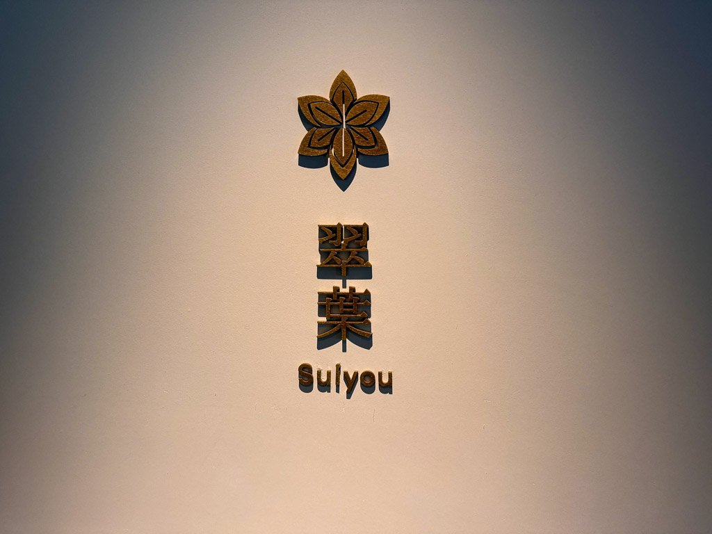  翠葉（Suiyou）のシンプルでエレガントなロゴ、壁に映える木製デザイン  Suiyou logo with a simple and elegant wooden design standing out on the wall 
