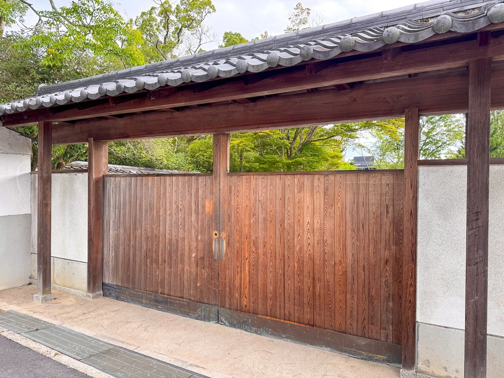  伝統的な日本建築の木製門、周囲の緑が美しい景観を作り出している  Traditional Japanese wooden gate with surrounding greenery creating a beautiful landscape 