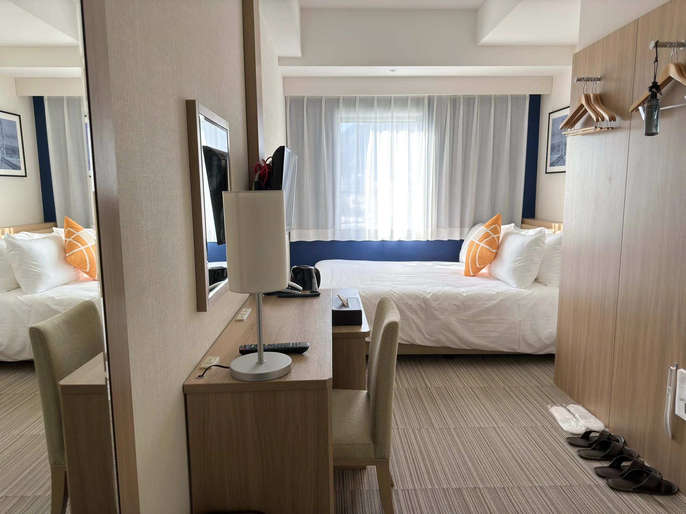 A Kobe Sannomiya double room with white bedding, orange cushions and a desk by the window