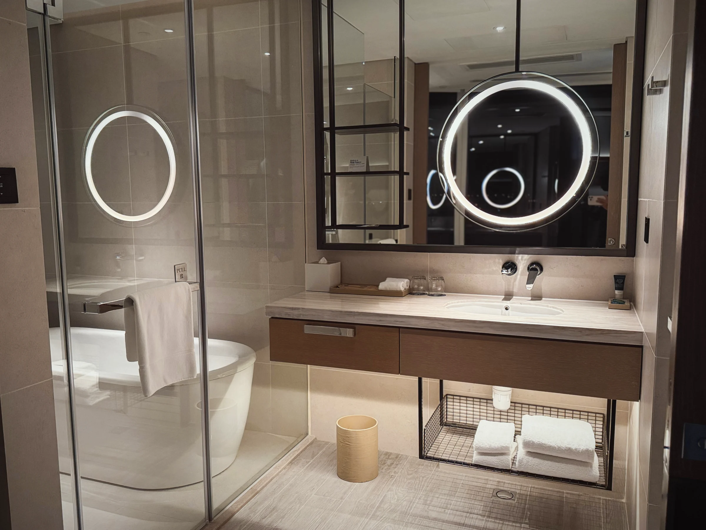 A round mirror and glass-enclosed bathroom