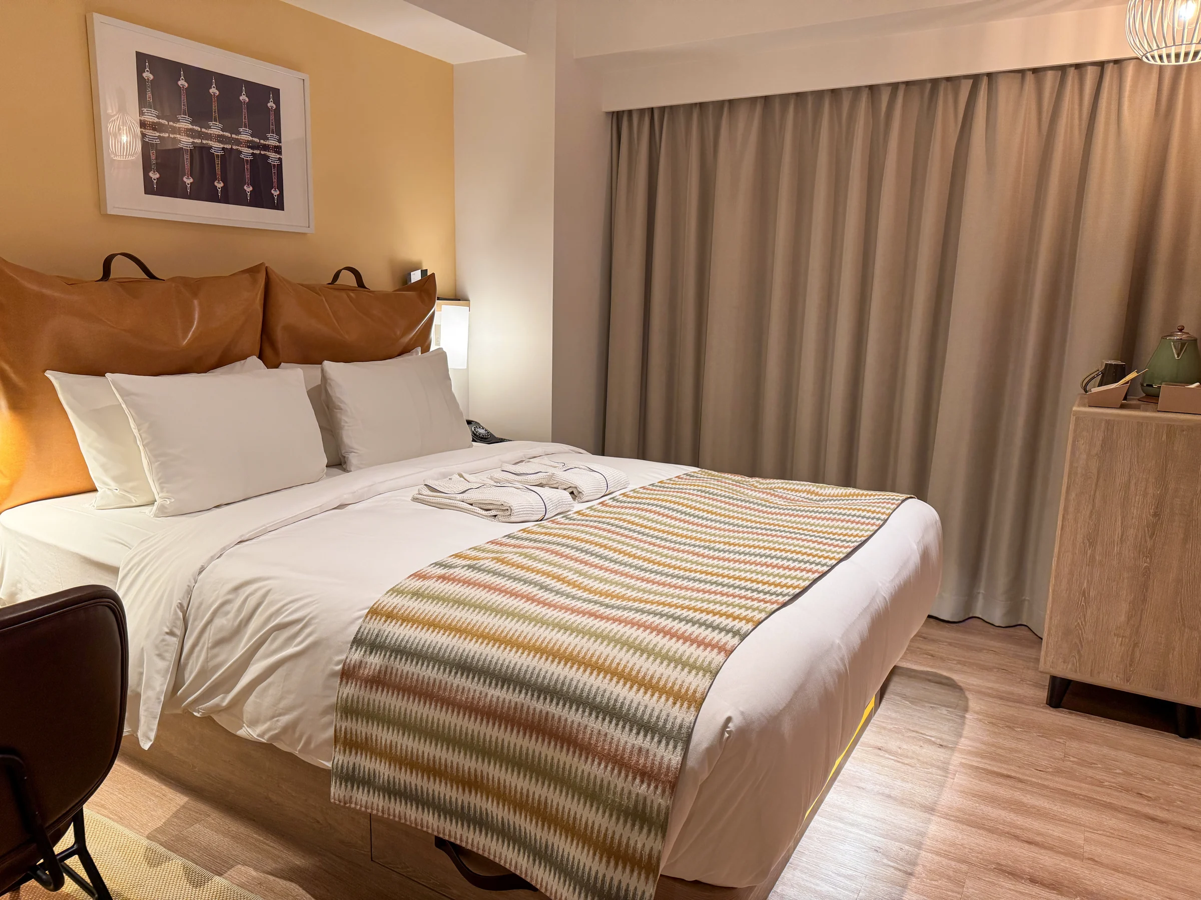 The Ume Queen room at Moxy Kyoto, with a striped bed cover, warm lighting and wall art