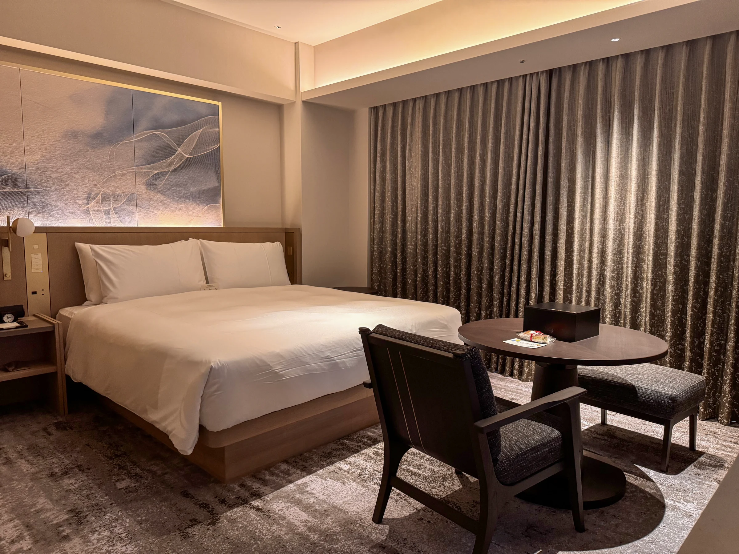 The Osaka Station Hotel's king bed, with curtains in calm colours and a round table