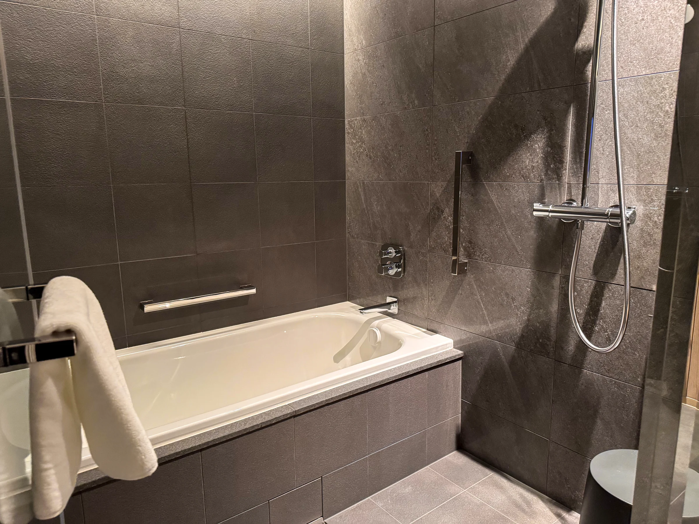 The bath and shower surrounded by grey tiles